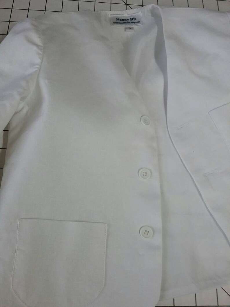 May include: White blazer with a v-neck and four buttons. The blazer has a pocket on the left side and a label that says "Nanny B's".