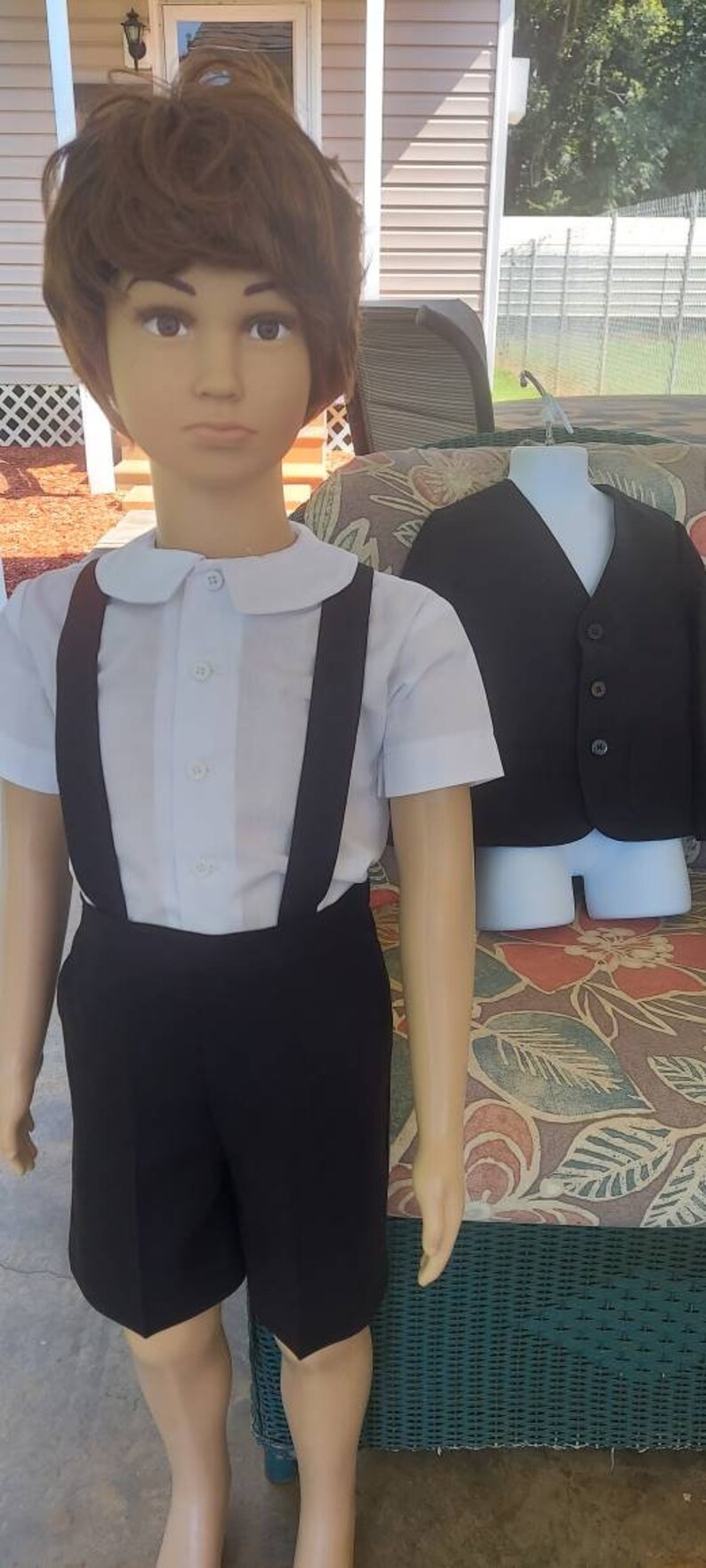 May include: A white collared shirt with black suspenders and black shorts. A black vest is on a mannequin in the background.