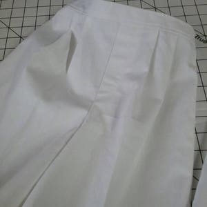 May include: White pleated pants with a single front pocket. The pants are made of a lightweight fabric and have a relaxed fit.