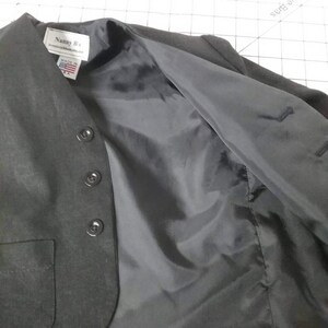 May include: A black blazer with a black lining and a pocket on the left side. The blazer has a label that reads "Nanny B's" and "Made in USA".