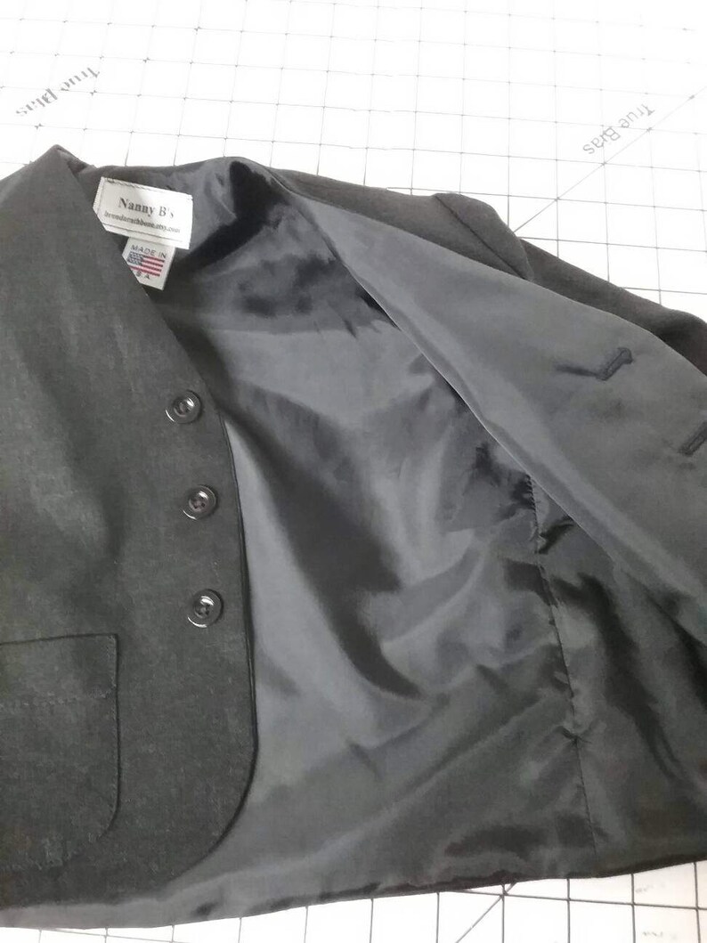 May include: A black blazer with a black lining and a pocket on the left side. The blazer has a label that reads "Nanny B's" and "Made in USA".