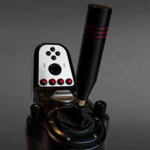 May include: A black gaming gear shifter featuring a tall, cylindrical handle with three horizontal red stripes. The base includes a silver control panel with a directional pad, four red buttons, and a black leather-like boot around the gear stick.