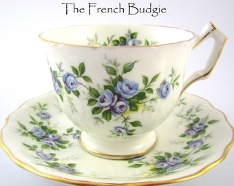 Può includere: Una tazza da tè e un piattino bianchi con un motivo floreale blu e verde. La tazza e il piattino hanno un bordo dorato.