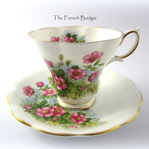 Peut inclure: Une tasse à thé et une soucoupe blanches avec un motif floral. La tasse et la soucoupe ont une bordure dorée. Le motif floral présente des fleurs roses et des feuilles vertes sur un fond bleu clair.