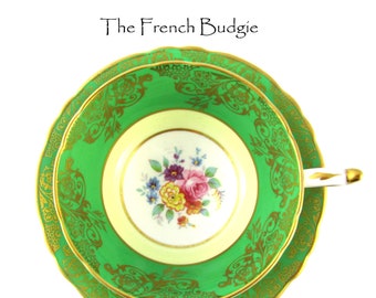 Puede incluir: Un juego de taza y platillo de té verde y dorado con un diseño floral. La taza y el platillo tienen un fondo blanco con un borde verde y detalles dorados.