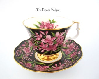 Puede incluir: Un juego de taza y platillo de té negro y blanco con diseños florales rosas. La taza y el platillo tienen un borde dorado.