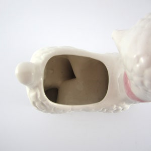 May include: White ceramic poodle planter with a pink ribbon around its neck. The planter has a hollow interior for planting.