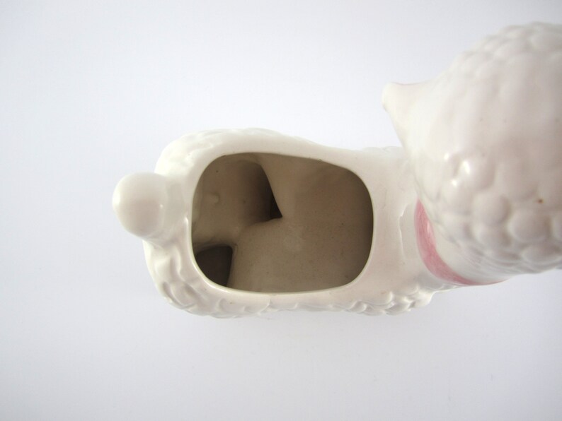May include: White ceramic poodle planter with a pink ribbon around its neck. The planter has a hollow interior for planting.