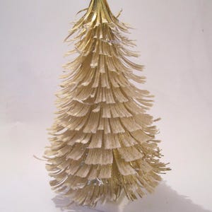 May include: A small, white, paper Christmas tree with gold tinsel and a white pom-pom on top.