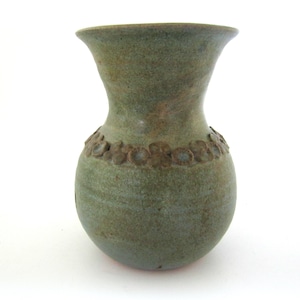 May include: A green ceramic vase with a bulbous body and flared rim. A band of floral relief decorates the neck. The vase has a textured surface and a matte finish, suitable for home decor.
