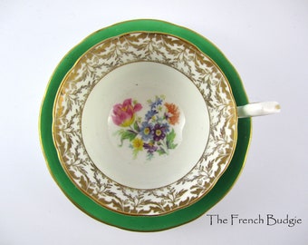Può includere: Un set vintage di tazza da tè e piattino con bordo verde e un motivo floreale dorato. La tazza presenta un delicato disegno floreale al centro.