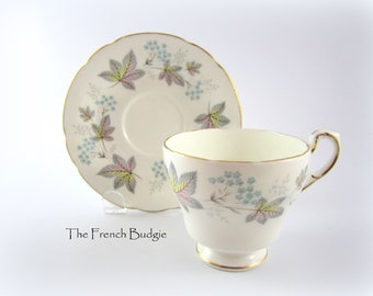 May include: A white teacup and saucer with a floral pattern featuring pink, green, and blue leaves. The cup and saucer have a gold trim.