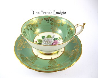Peut inclure: Une tasse à thé et une soucoupe vertes avec des bordures dorées et des motifs floraux. La tasse et la soucoupe sont toutes deux décorées d'un motif floral délicat dans des tons de rose, blanc et vert. La bordure dorée ajoute une touche d'élégance au design.