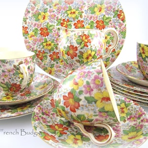 May include: A vintage floral tea set with a cream base and a colourful floral pattern. The set includes a teapot, creamer, sugar bowl, cups, and saucers.