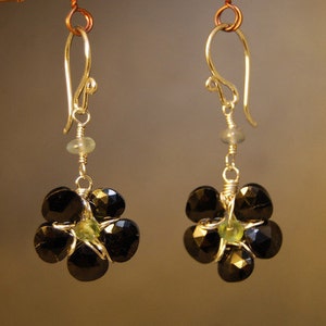 May include: A pair of earrings with black and green gemstone accents. The earrings are made of silver and have a flower-shaped design.