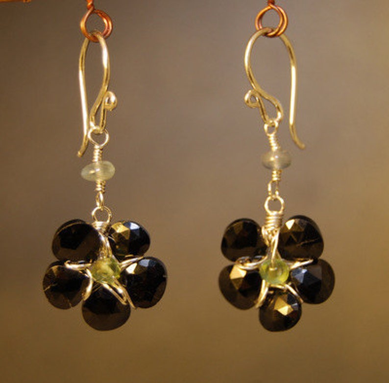 May include: A pair of earrings with black and green gemstone accents. The earrings are made of silver and have a flower-shaped design.