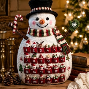 May include: A white crocheted snowman advent calendar featuring a black top hat, a red, green, and white striped scarf, and twenty-four red pockets numbered one through twenty-four, each containing a small crocheted holiday figure.