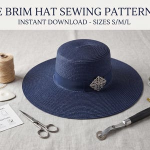 May include: A navy blue wide brim hat with a matching ribbon and a silver decorative brooch. The image includes text reading WIDE BRIM HAT SEWING PATTERN PDF INSTANT DOWNLOAD - SIZES S/M/L, a spool of thread, a white tailor's chalk, scissors, a measuring tape, a tracing wheel, and a paper instruction sheet.