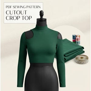 Puede incluir: Un top corto de manga larga en color verde oscuro con cuello alto y aberturas en los hombros sobre un maniquí. La imagen incluye el texto PDF SEWING PATTERN CUTOUT CROP TOP, una tela verde doblada, carretes de hilo y una cinta métrica.