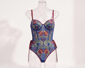 Puede incluir: Un patrón de costura PDF para un body azul con un intrincado diseño bordado de granadas y enredaderas en rojo, verde y dorado. La prenda tiene tirantes finos, escote corazón y lazos laterales. Texto: BODYSUIT SEWING PATTERN PDF. Tallas: US 2-16.