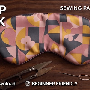 May include: A sleep mask sewing pattern PDF featuring a geometric print in shades of pink, mustard yellow, and dark gray. The mask has a purple elastic strap and is displayed with metal sewing scissors, a needle, and thread. Text includes SLEEP MASK, SEWING PATTERN PDF, Instant Download, BEGINNER FRIENDLY, and Size: Adult.