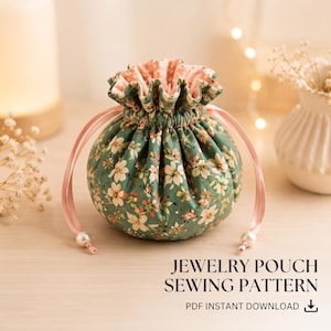 Può includere: Un sacchetto rotondo in tessuto con coulisse, esterno verde con motivo floreale bianco e rosa, fodera interna rosa chiaro e due nastri di raso rosa chiaro con perline bianche alle estremità. Il testo recita: JEWELRY POUCH SEWING PATTERN PDF INSTANT DOWNLOAD.
