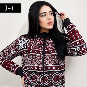 May include: A long-sleeved zip-up jacket featuring a dark red, black, and white geometric and floral pattern. The garment includes a black ribbed collar, black ribbed cuffs, and a black ribbed hem. The text J-1 is visible in the top left corner.