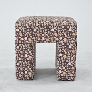 May include: A square-shaped stool upholstered in a dark brown fabric featuring a dense, repeating pattern of small flowers in shades of white, light pink, yellow, and muted green. The stool has a solid, block-like structure with four legs.