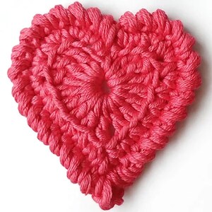 Può includere: Un'applicazione all'uncinetto a forma di cuore realizzata con filato rosa vivace. Il pezzo presenta un motivo a punti denso e strutturato con un'apertura centrale visibile e un bordo in rilievo in stile intrecciato lungo tutto il perimetro.