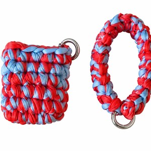 May include: A rectangular crochet pouch and a matching oval wrist strap, both crafted from red and light blue fabric strips. The pouch features a silver metal ring at the top corner, while the wrist strap includes a silver metal ring at the base.
