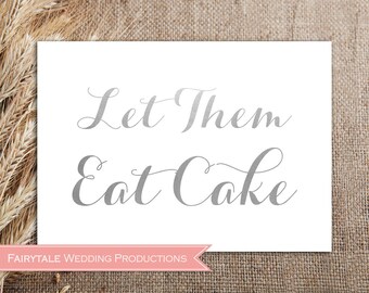 May include: A white sign with the text "Let Them Eat Cake" in silver script. The sign has a pink banner at the bottom with the text "Fairytale Wedding Productions".