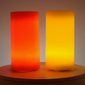 May include: Two cylindrical lamps, one red and one yellow, are lit and glowing on a white circular surface.