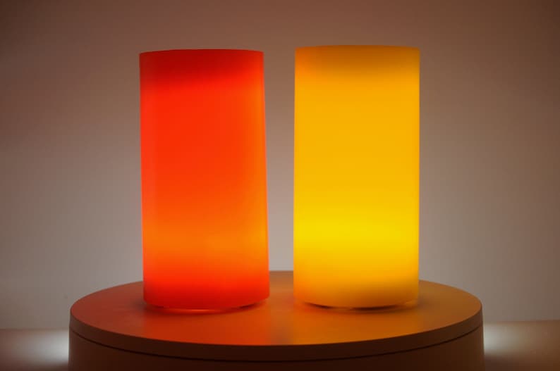 May include: Two cylindrical lamps, one red and one yellow, are lit and glowing on a white circular surface.