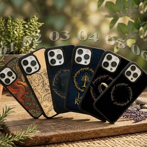 May include: Six smartphone cases arranged in a row, featuring various designs including a red dragon, a map, a golden tree, and the One Ring with Elvish script. Each case has a black frame and a cutout for a multi-lens camera system.