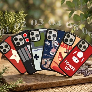 May include: Six smartphone cases arranged in a row, featuring various designs including a red star, a game controller layout, a handheld console graphic with Nintendo Game Boy text, a space scene, a retro video game theme, and a red case with a mushroom icon and the text POWER UP.