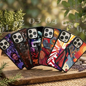 May include: A collection of six smartphone cases featuring colourful graphic illustrations of characters and scenes from the Guardians of the Galaxy, each with a black frame and a triple-lens camera cutout, arranged in a row on a wooden surface.