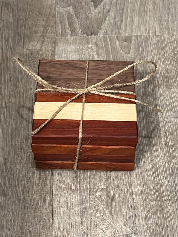 A set of 4 coasters cut from three distinct hardwoods — walnut, maple, and African padauk — so no two look alike and the contrast is genuinely striking.