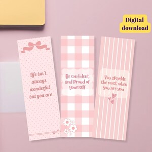 May include: Three rectangular bookmarks in shades of pink. The first features a bow and the text 'Life isn't always wonderful but you are'. The second has a gingham pattern and the text 'Be confident and Proud of yourself'. The third has stripes and the text 'You sparkle the most when you are you'.