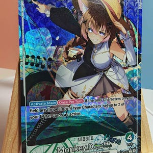 Puede incluir: Una carta coleccionable holográfica de One Piece con un personaje de anime de cabello castaño y orejas de gato que lleva un sombrero de paja. La carta muestra el texto Monkey.D.Luffy, Leader, 5000 power e instrucciones de juego sobre un fondo azul.