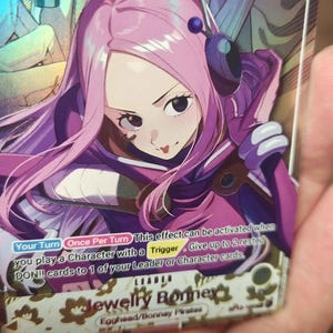May include: A holographic trading card featuring the character Jewelry Bonney with long pink hair, wearing a purple outfit and a headset. The card displays the text 5000, Special, Your Turn, Once Per Turn, Trigger, DON!!, LEADER, and Jewelry Bonney.