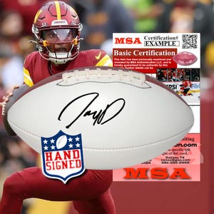 Pode incluir: Uma bola de futebol americano de couro branco com um autógrafo em tinta preta no centro, acompanhada por um adesivo azul e branco em forma de escudo com a etiqueta HAND SIGNED e um certificado MSA com código QR e informações de contato.