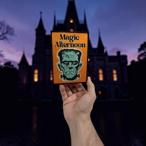 Könnte beinhalten: Ein rechteckiger Aufnäher mit orangefarbenem Hintergrund, der den Text Magic Afternoon in schwarzen Buchstaben über einer grünen Illustration eines Monstergesichts mit Stichen auf der Stirn und Metallbolzen am Hals zeigt.