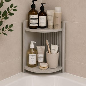 Puede incluir: Una estantería de esquina para ducha de color gris con dos niveles y un panel trasero vertical acanalado. El estante superior contiene cuatro botellas de varias marcas. El estante inferior contiene un frasco con bomba, dos tubos y un cepillo.