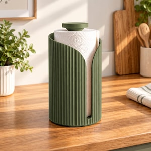 May include: A cylindrical olive green paper towel holder featuring a vertical ribbed texture and a matching circular top knob. The holder is open on one side to reveal a roll of white paper towels with a subtle embossed floral pattern.