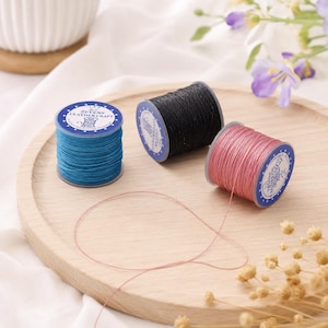 May include: Three spools of waxed thread in blue, black, and pink. Each spool has a circular blue label with white text reading ZEVENS LEATHER CRAFT and a small icon of a spool. The pink thread is partially unspooled, creating a thin loop on the surface.