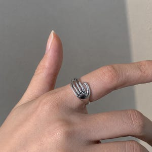 Moderner offener Fingerring, gestaltet wie eine ruhende Hand, die Ruhe und Gelassenheit symbolisiert. Ideal zum Kombinieren mit anderen Schmuckstücken im Alltag.