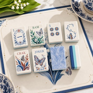 May include: A set of eight rectangular mahjong tiles featuring white surfaces with blue, green, and red printed designs. The tiles display various illustrations including butterflies, floral patterns, the number 5, and the text 1, BAM, CRAK, and JOKER.