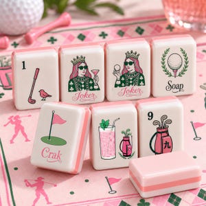May include: A set of cream-colored Mahjong tiles featuring pink and green golf-themed illustrations and text. Designs include a golf club, a queen wearing sunglasses labeled Joker, a golf ball labeled Soap, a flag labeled Crak, and a golf bag.