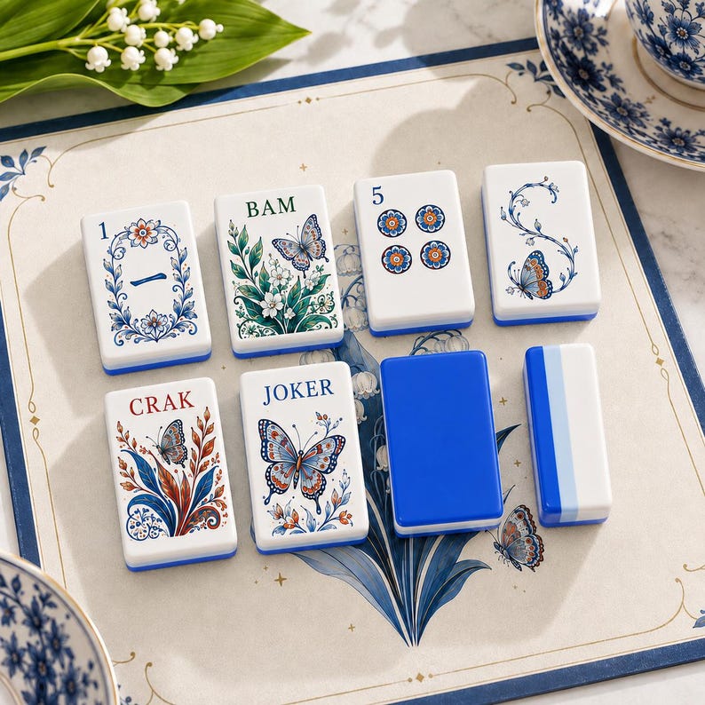 May include: A set of eight rectangular mahjong tiles featuring white surfaces with blue, green, and orange illustrations of butterflies, floral patterns, and text including 1, BAM, 5, and JOKER. Some tiles have solid blue backs or sides.