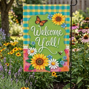 A colorful garden sign with a welcoming message, surrounded by flowers and greenery.